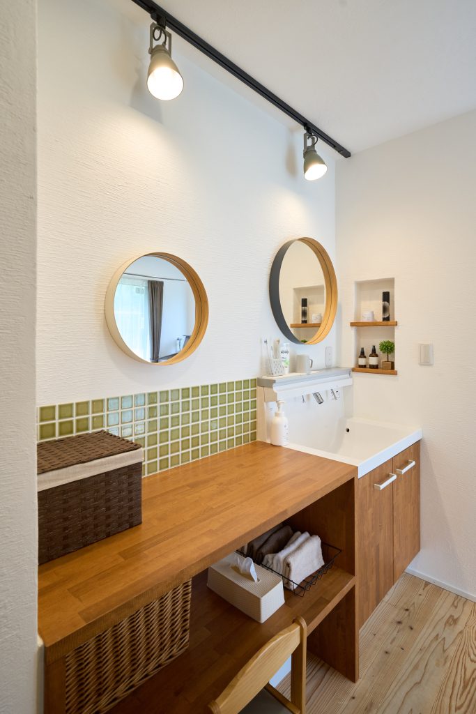 丸い鏡が印象的な洗面室。造作洗面台の横には土間とおそろいのグリーンのタイルが。